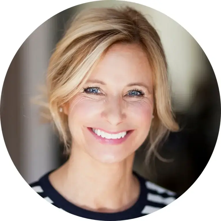 Person with loose blonde waves smiles at the camera, wearing a dark top with white horizontal stripes.