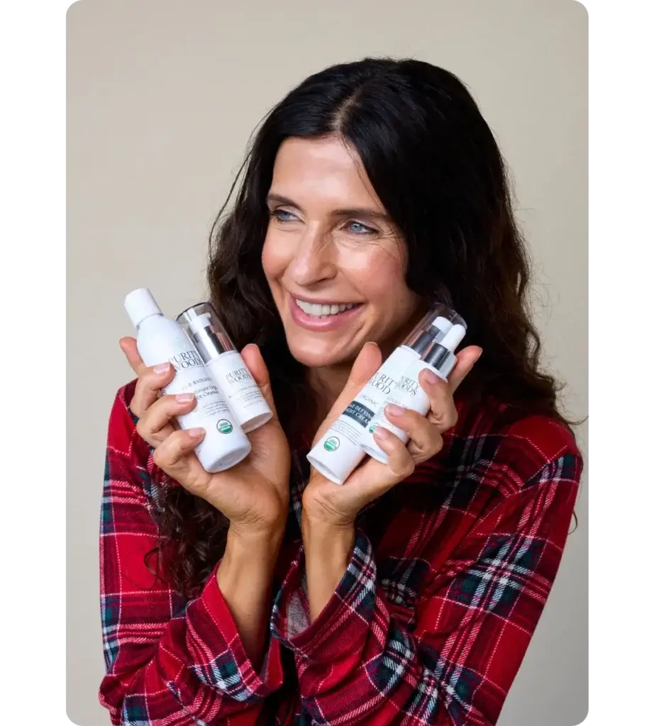 Smiling woman in a red plaid shirt holding four Purity Woods organic skincare products